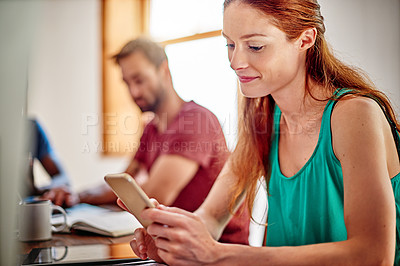 Buy stock photo Shot of a young woman sitting at a desk in an office using a digital tablet with colleagues in the background