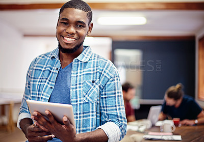 Buy stock photo Portrait of a smiling young man standing in an office using a digital tablet with colleagues in the background
