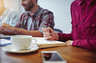 Buy stock photo Closeup shot of a woman writing on a notepad with colleagues at work in the background