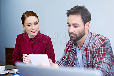 Buy stock photo Shot of two colleagues talking together over a digital tablet while working in an office