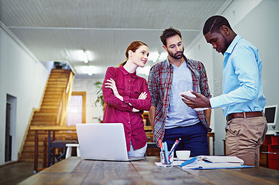 Buy stock photo Shot of a group of colleagues talking together over a digital tablet while standing in an office