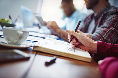 Buy stock photo Closeup shot of a woman writing on a notepad with colleagues at work in the background