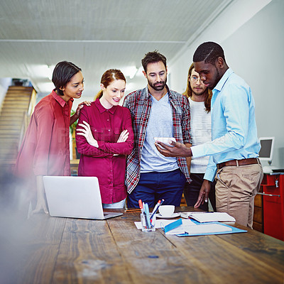 Buy stock photo Shot of a group of colleagues talking together over a digital tablet while standing in an office