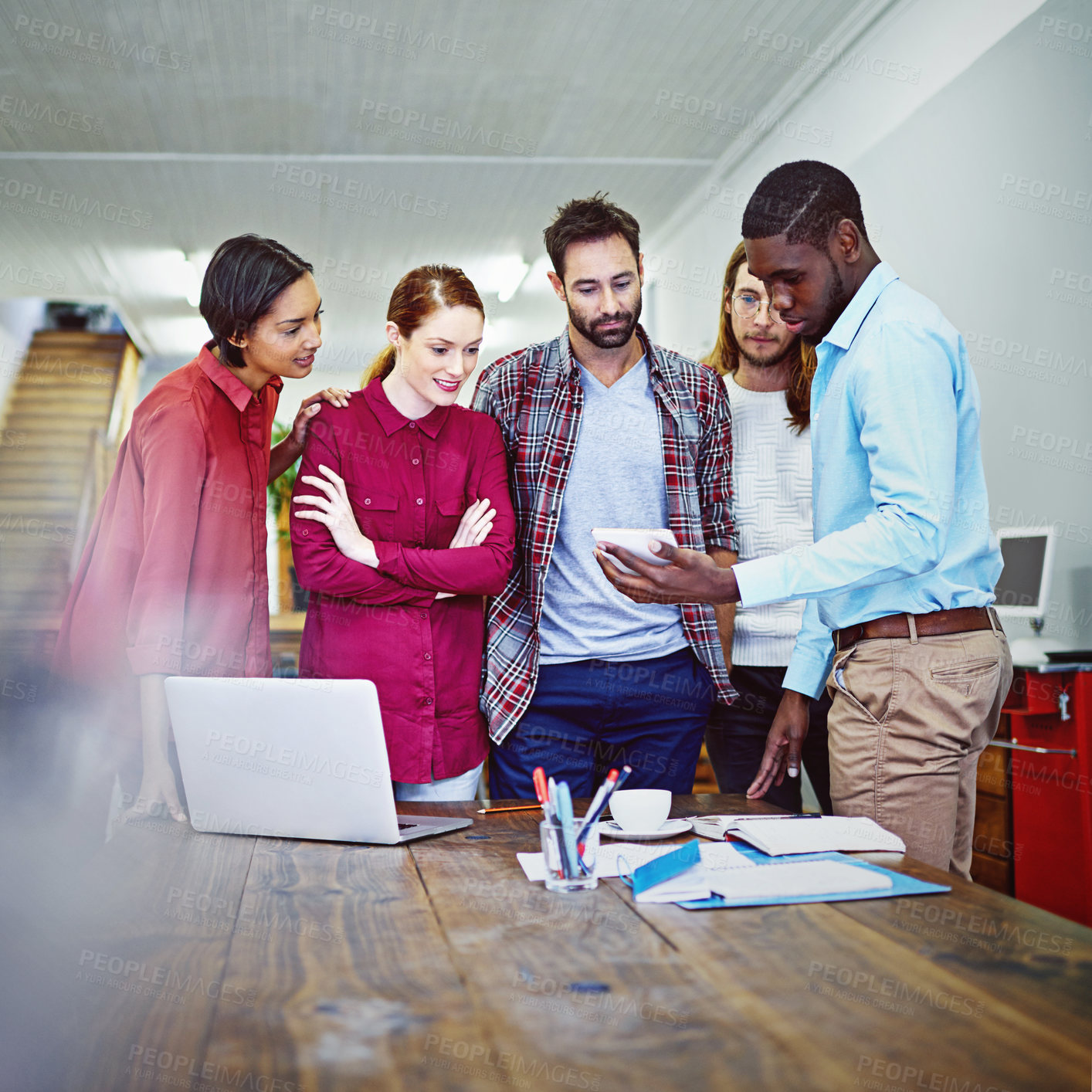 Buy stock photo Shot of a group of colleagues talking together over a digital tablet while standing in an office