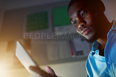 Buy stock photo Shot of a young man working on a digital tablet in an office in the evening
