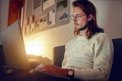 Buy stock photo Shot of a young designer working on a laptop in an office late in the evening