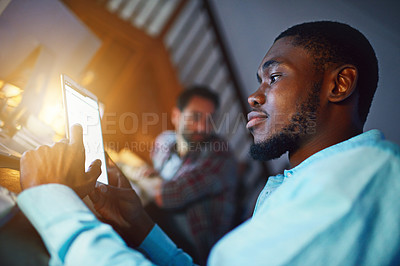 Buy stock photo Shot of a man working on a digital tablet in an office in the evening with colleagues in the background