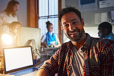 Buy stock photo Portrait of a smiling man working on a laptop in an office in the evening