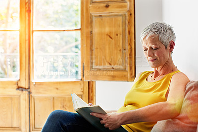 Buy stock photo Shot of a mature woman relaxing on her sofa at home reading a book