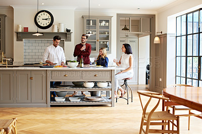 Buy stock photo Shot of a group of friends talking and drinking wine while preparing a meal together