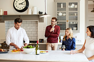 Buy stock photo Shot of a group of friends talking and drinking wine while preparing a meal together