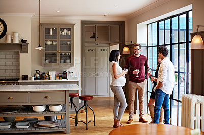Buy stock photo Shot of a group of friends drinking wine and talking together in a kitchen at a get-together