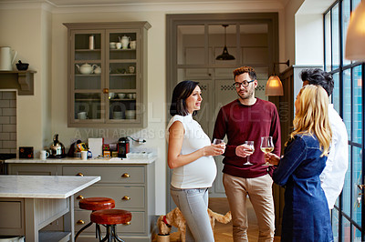 Buy stock photo Shot of a group of friends drinking wine and talking together in a kitchen at a get-together