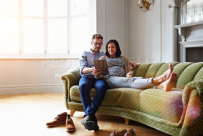Buy stock photo Shot of a pregnant woman and her husband sitting on their sofa using a digital tablet