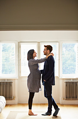 Buy stock photo Shot of a happy pregnant couple standing face to face together in their home