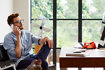 Buy stock photo Shot of a young man talking on a cellphone while sitting in his home office