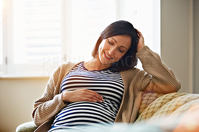 Buy stock photo Shot of a smiling pregnant woman sitting on her sofa holding her stomach
