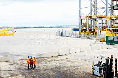 Buy stock photo High angle shot of three workers talking together while standing on a commercial dock