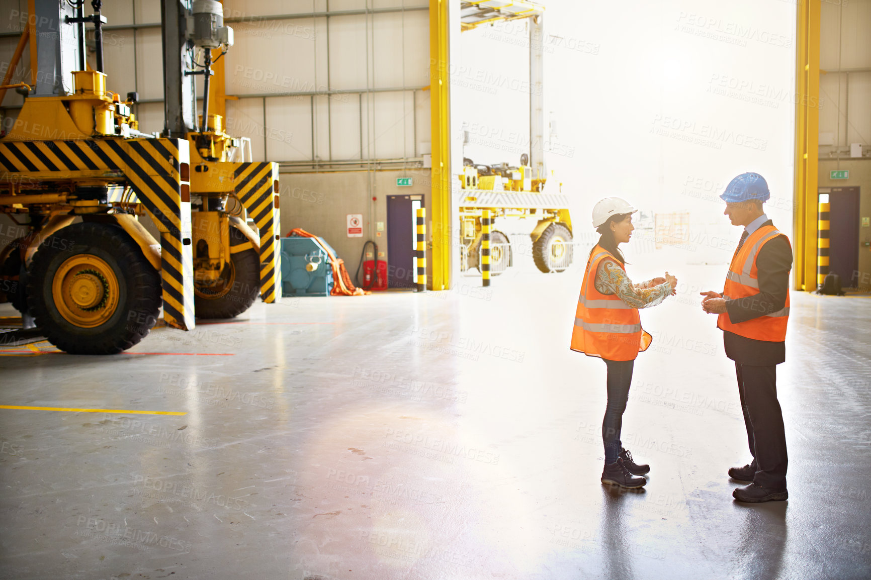 Buy stock photo Shot of two warehouse workers talking together inside of a large warehouse