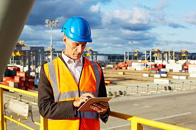 Buy stock photo Shot of a man in workwear standing on a walkway using a digital tablet over at a large commercial dock