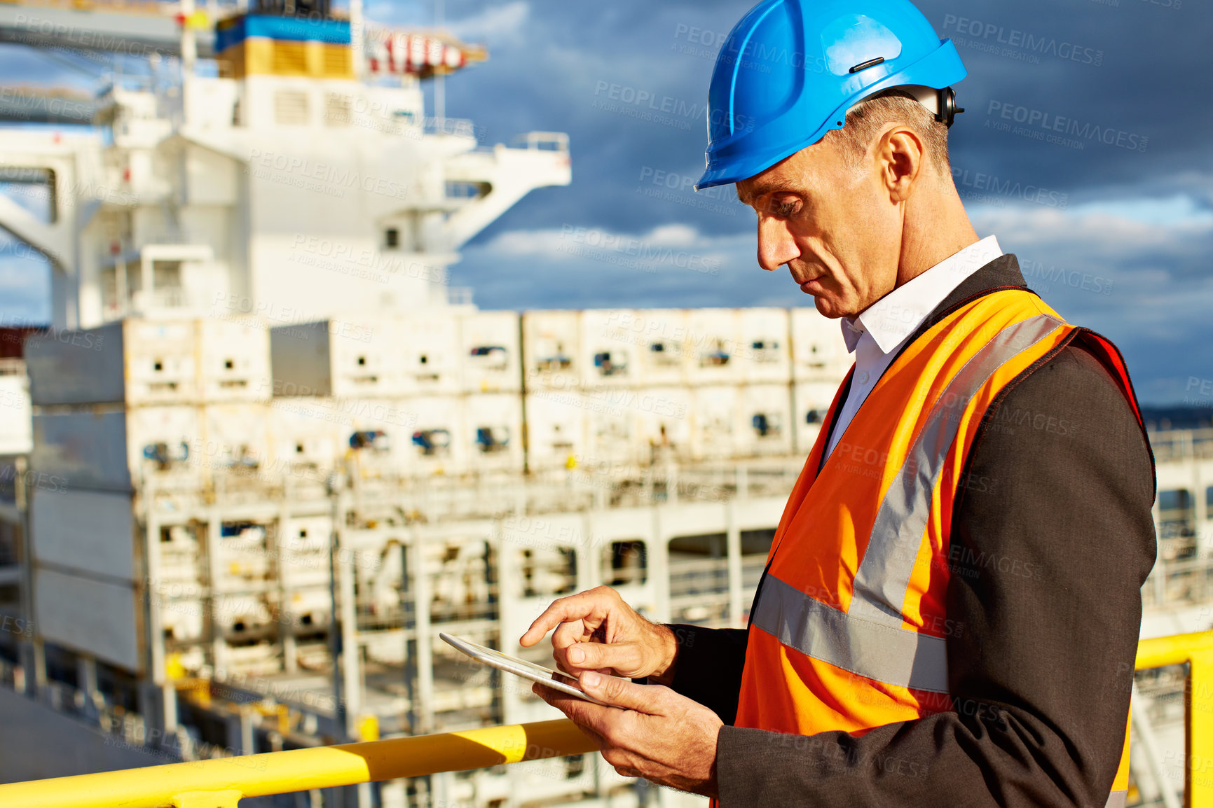 Buy stock photo Shot of a man in workwear standing on a walkway using a digital tablet over at a large commercial dock