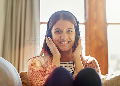 Buy stock photo Portrait of a smiling young woman sitting on her sofa listening to music on headphones