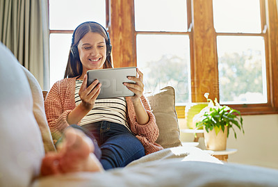 Buy stock photo Shot of a smiling young woman sitting on her sofa watching a movie on a digital tablet with headphones