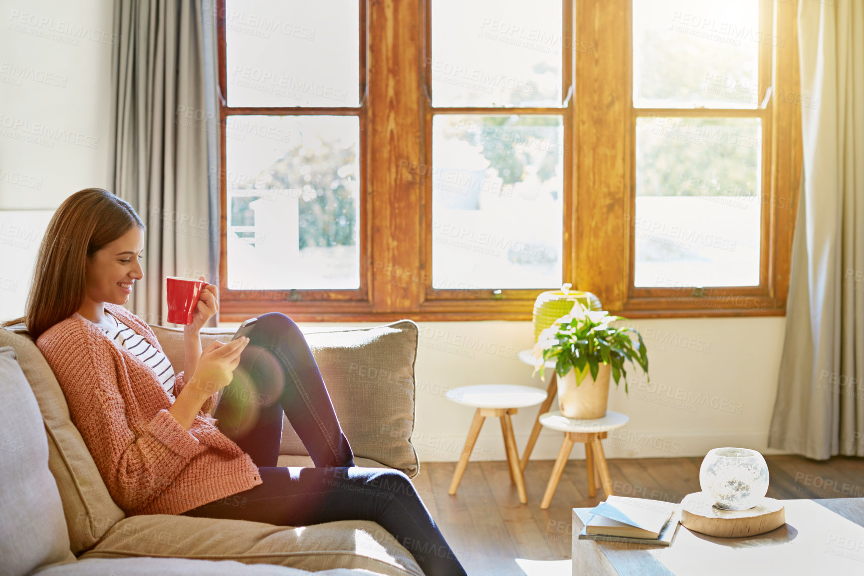 Buy stock photo Shot of a young woman sitting on her living room sofa drinking a coffee and using a cellphone