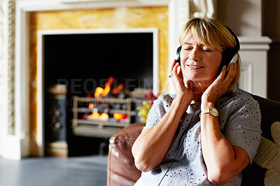 Buy stock photo Shot of a mature woman sitting back on her sofa listening to music on headphones