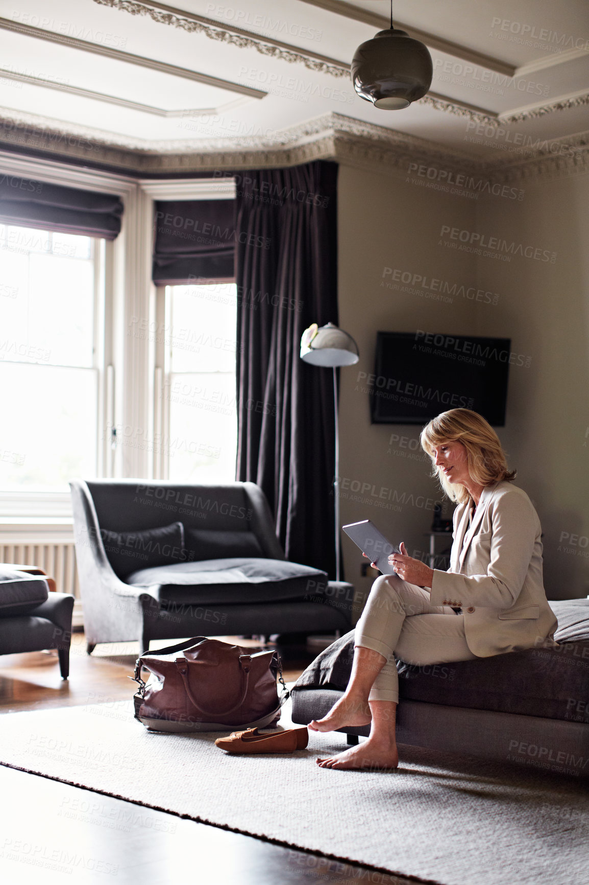 Buy stock photo Shot of a mature businesswoman sitting on a hotel bed using a digital tablet