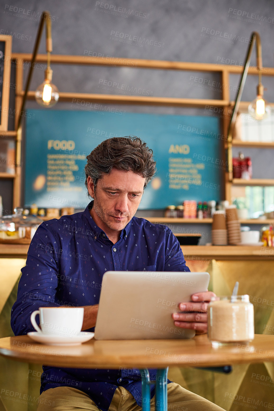 Buy stock photo Shot of a man working on a digital tablet in a cafe