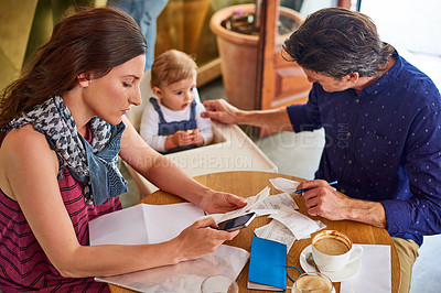 Buy stock photo Shot of a woman going through bills at a cafe with her husband and baby girl next to her