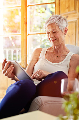 Buy stock photo Shot of a mature woman relaxing on her sofa at home using a digital tablet