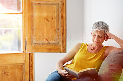 Buy stock photo Shot of a mature woman relaxing on her sofa at home reading a book