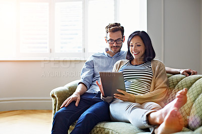Buy stock photo Shot of a pregnant woman and her husband sitting on their sofa using a digital tablet