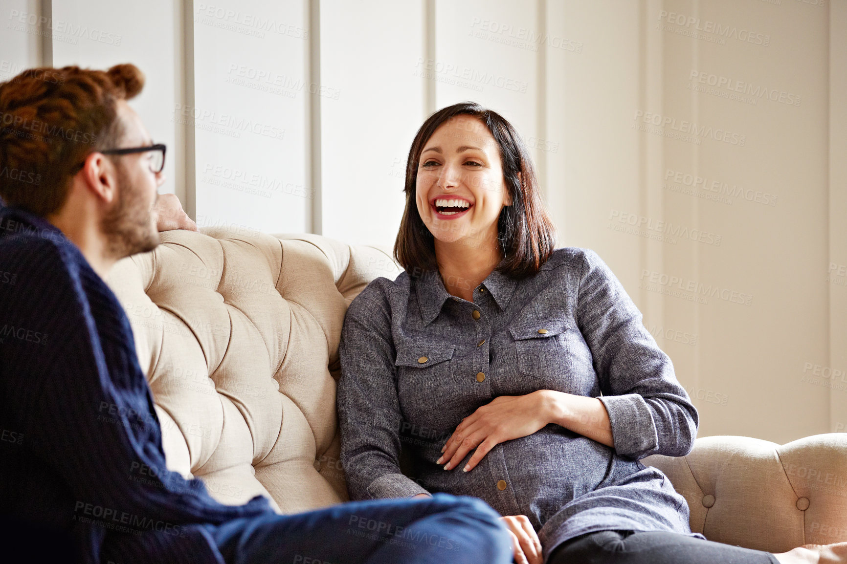 Buy stock photo Shot of a young expecting couple talking together while sitting on the sofa at home