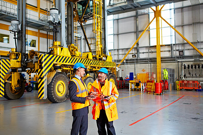 Buy stock photo Shot of two warehouse workers talking together inside of a large warehouse