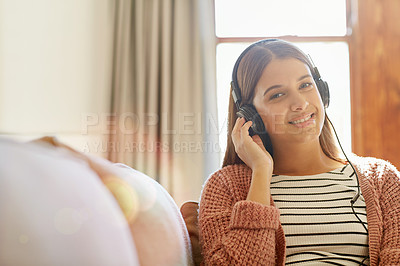 Buy stock photo Portrait of a smiling young woman sitting on her sofa listening to music on headphones