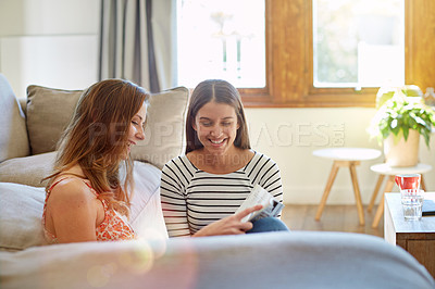 Buy stock photo Shot of two young friends sitting on the living room floor reading a magazine and talking together