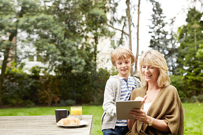 Buy stock photo Shot of a grandmother and her grandson using a digital tablet while eating lunch at a table in her yard