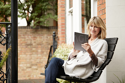 Buy stock photo Shot of a mature woman sitting on a bench on her front porch using a digital tablet