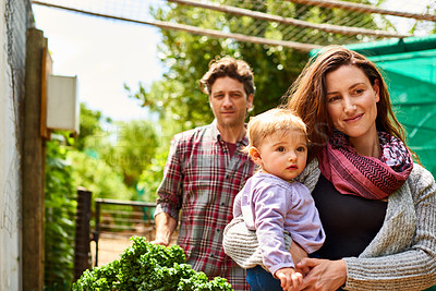 Buy stock photo Shot of a couple with their baby girl standing in their organic garden