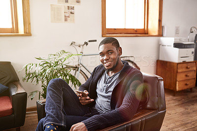 Buy stock photo Portrait of a smiling young man using a cellphone while sitting in an office