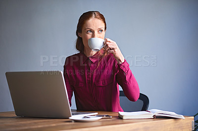 Buy stock photo Shot of a young woman drinking a cup of coffee while working on a laptop at a desk in an office