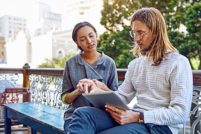Buy stock photo Shot of two young designers sitting together on a bench outside of their office using a digital tablet