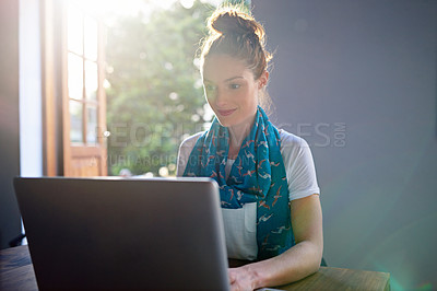Buy stock photo Shot of a young woman sitting by an open door in an office working on a laptop