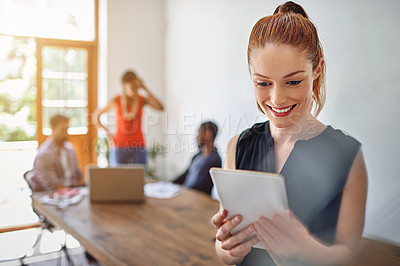 Buy stock photo Shot of a smiling young woman using a digital tablet in an office with colleagues in the background