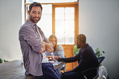 Buy stock photo Portrait of a smiling man standing in an office with colleagues working in the background
