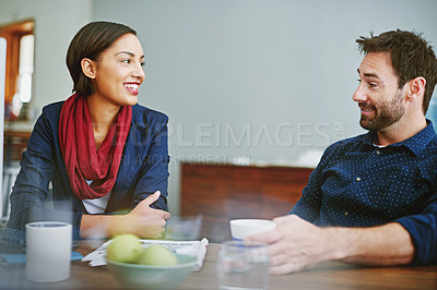 Buy stock photo Shot of two smiling colleagues talking together while sitting at a desk in an office