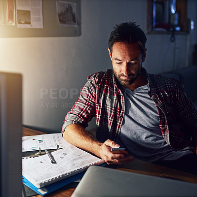 Buy stock photo Shot of a man using a cellphone and working on a laptop in an office in the evening